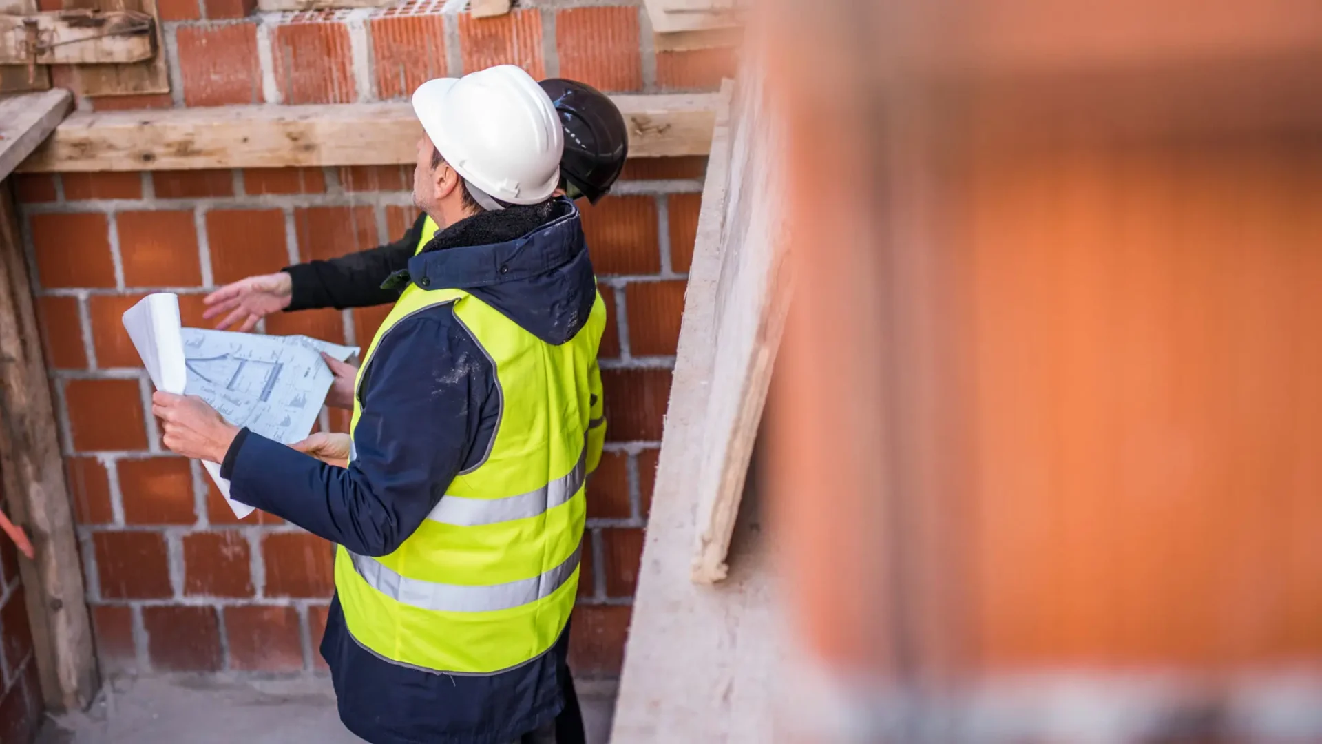 Construction workers discussing plans on a brick building site.