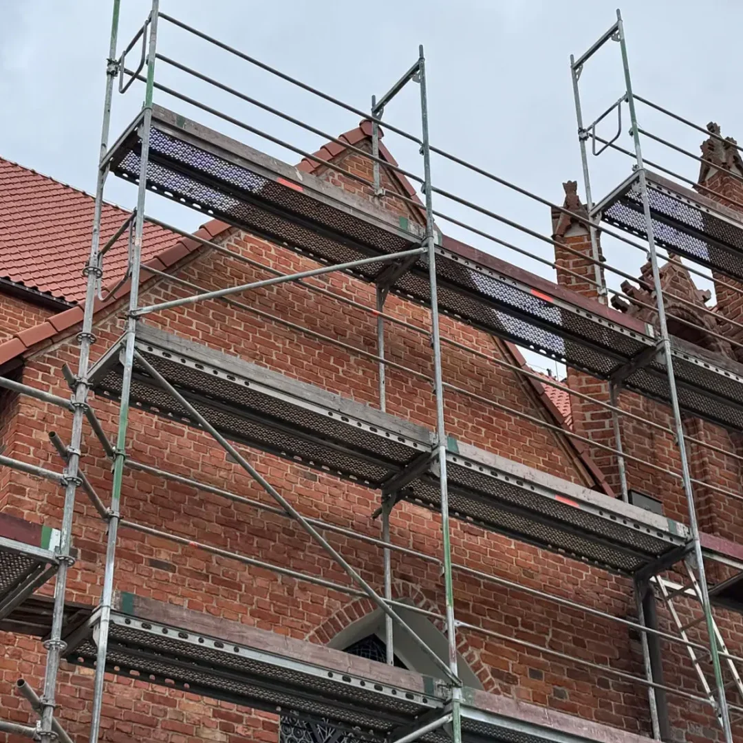 Metal scaffolding set up against a brick building with a tiled roof.