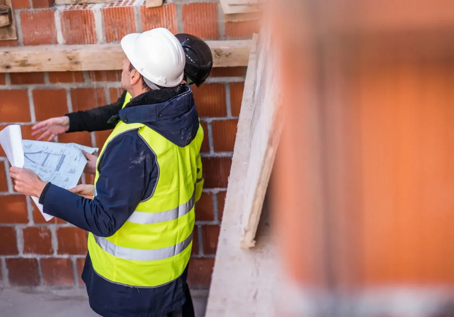 Construction workers discussing plans on a brick building site.