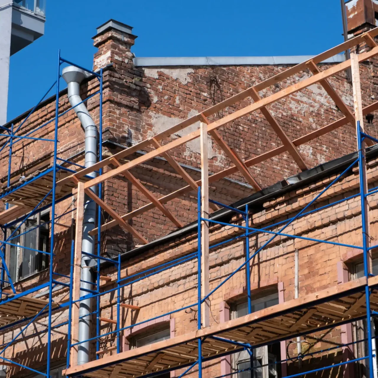 Scaffolding set up around a brick building under renovation on a clear day.